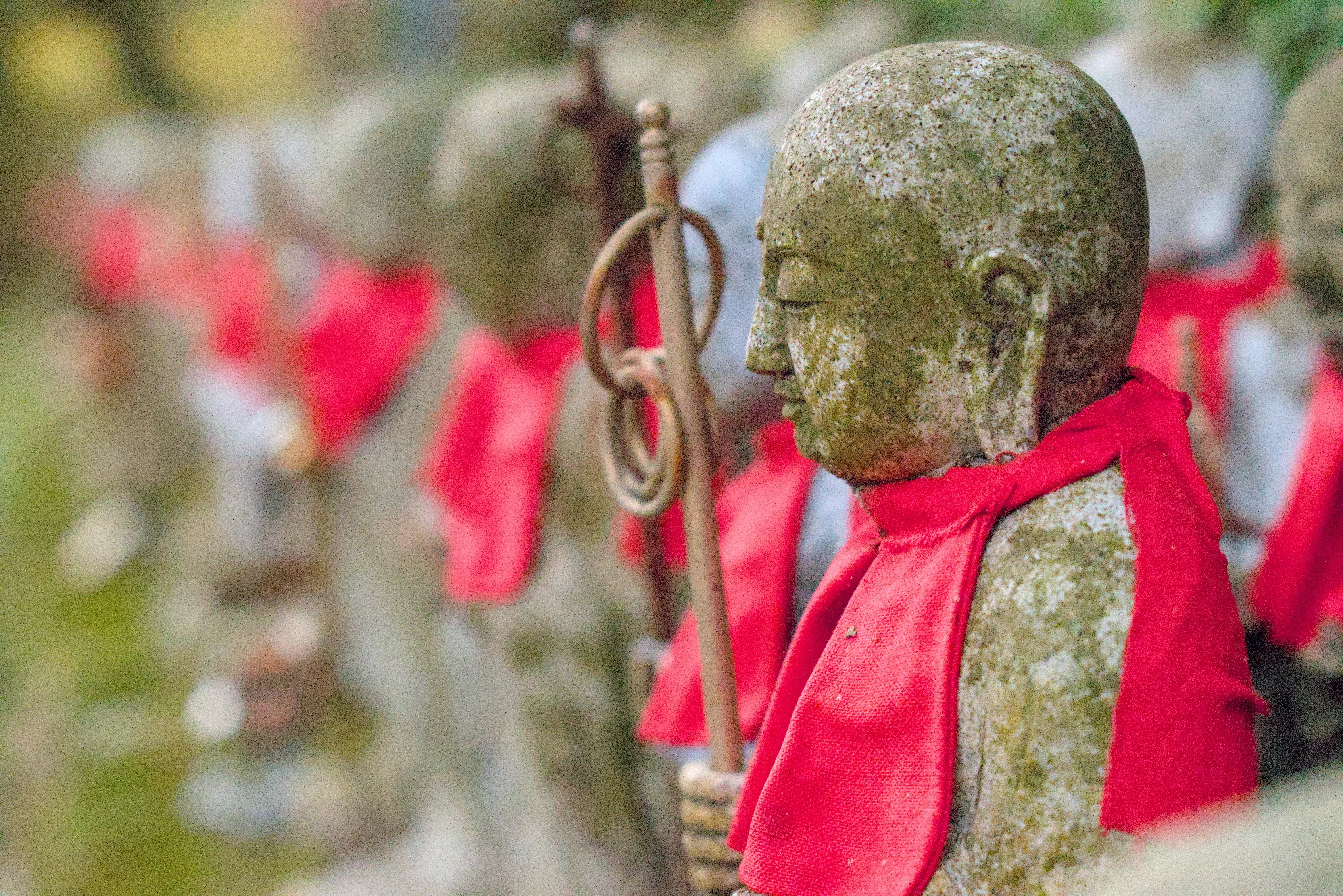 Jizo Buddhist statues in a forest are often decorated with red bibs as a prayer for deceased babies and as a protection against evil.